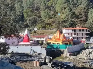 Neem Karoli Baba Mandir nestled in the Himalayan hills with colorful temple structures surrounded by forested mountains.
