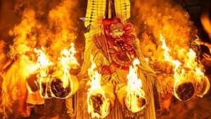 Kandakarnan Theyyam adorned with a towering headdress and traditional costume performs amid blazing torches during a nighttime ritual at a sacred village shrine in Kannur, Kerala.