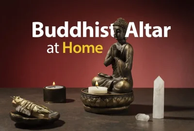Home Buddhist altar setup featuring a meditating Buddha statue, lit candles, sage bundle, and crystal on a wooden table with the text ‘Buddhist Altar at Home’