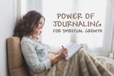 Woman sitting by a window, wrapped in a cozy blanket, smiling while writing in a notebook—practicing spiritual journaling