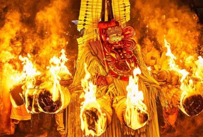Kandakarnan Theyyam adorned with a towering headdress and traditional costume performs amid blazing torches during a nighttime ritual at a sacred village shrine in Kannur, Kerala.